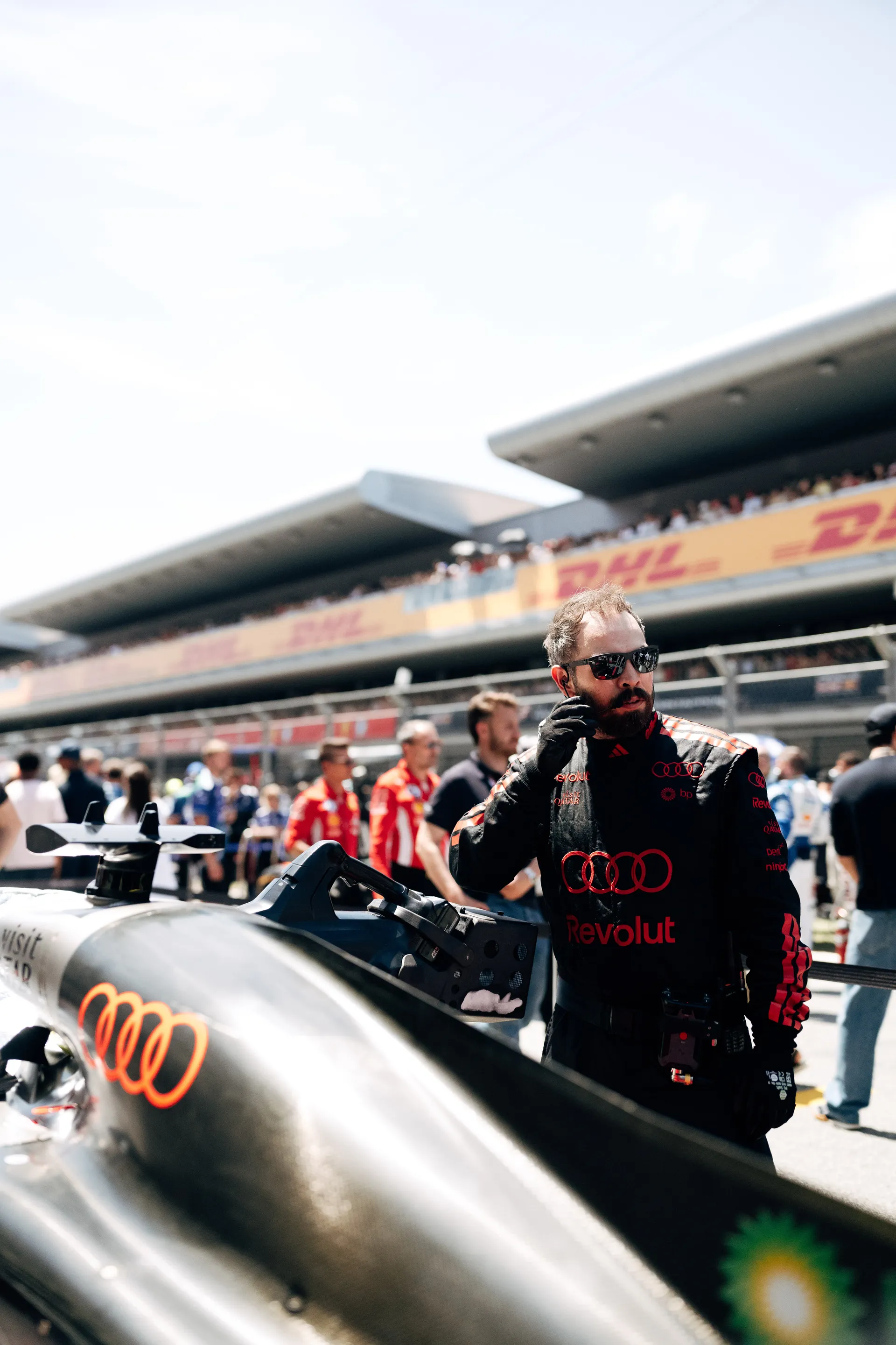 Audi Revolut F1® Team crew member adjusting equipment beside the Audi R26 on the grid during pre-race setup.