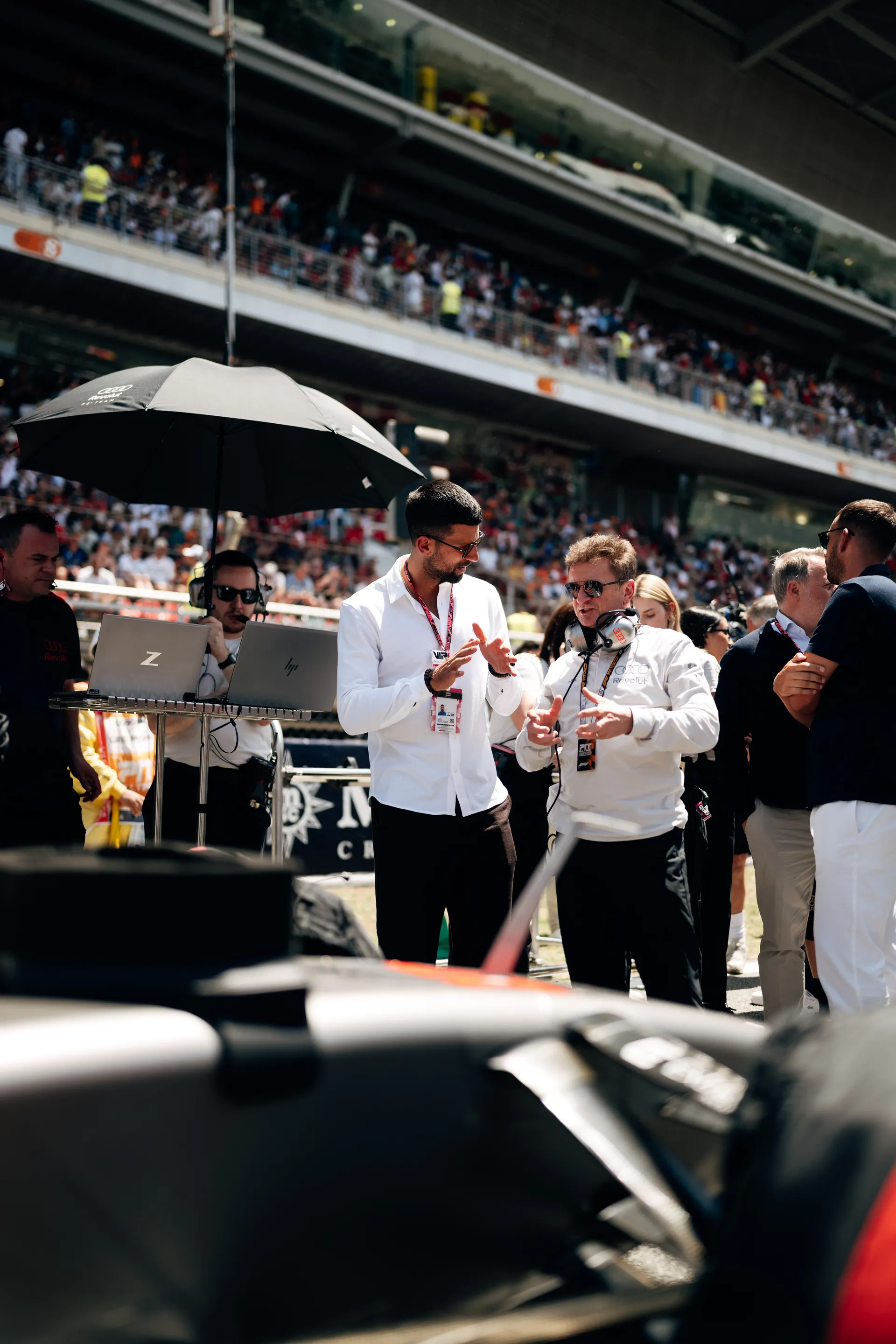 Allan McNish in conversation on the grid with Novak Đoković, surrounded by team members and media ahead of the race start.
