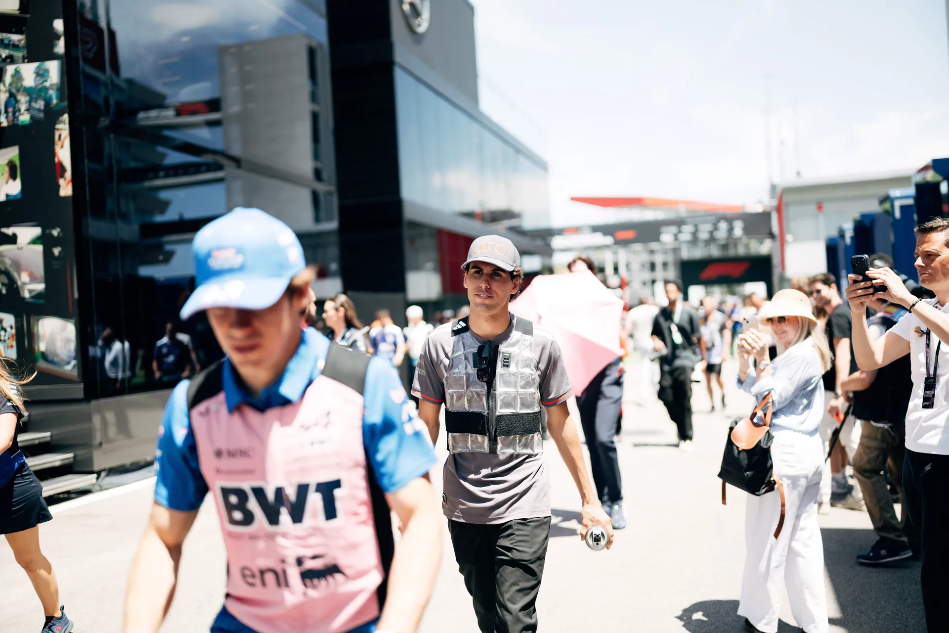 Gabriel Bortoleto walking through the paddock holding a drink, surrounded by fans and team personnel during the Barcelona race weekend