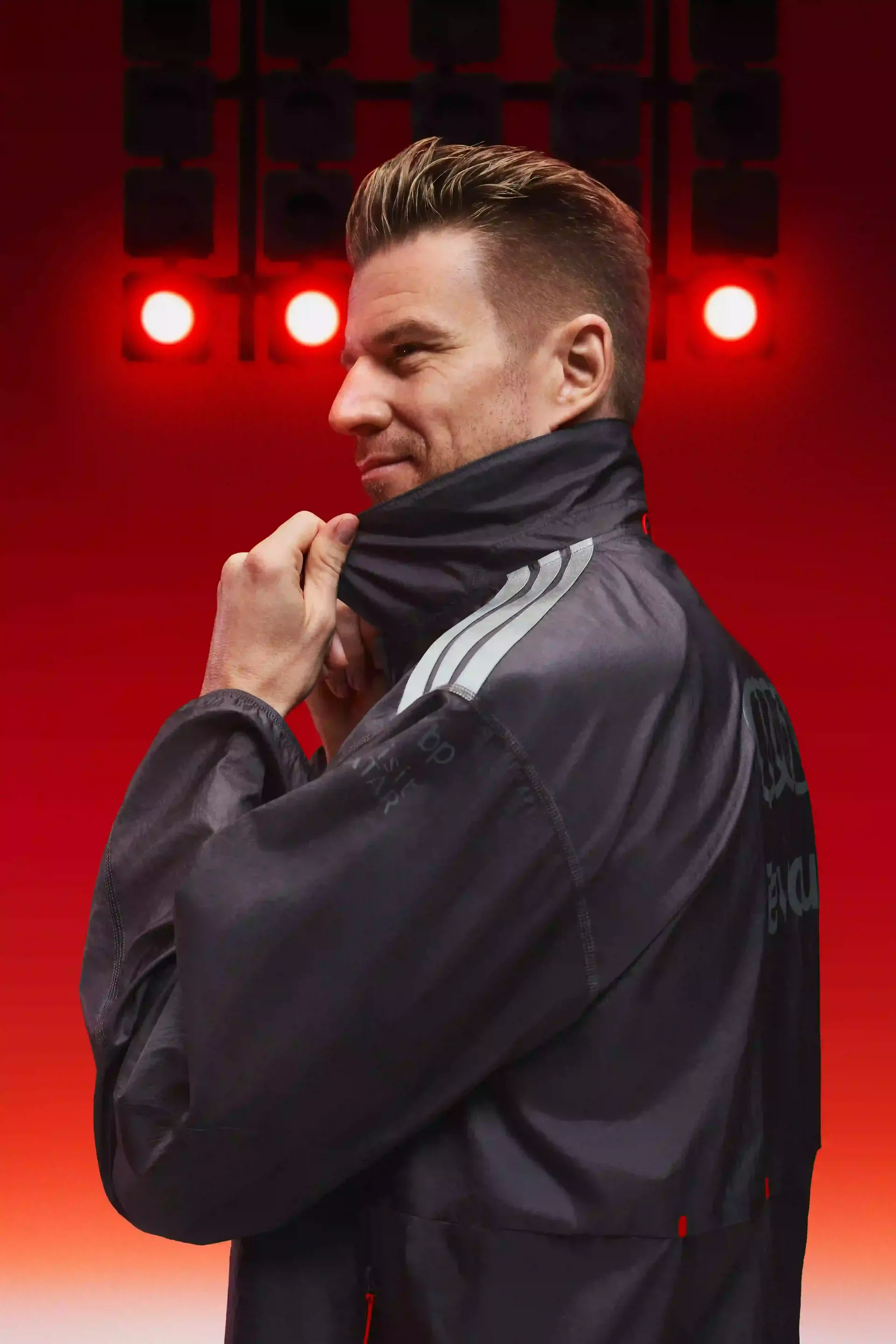 Formula 1® driver Nico Hulkenberg dark grey team jacket with adidas Audi Revolut F1® Team branding three quarter portrait hand on collar confident posture red background symmetrical racing lighting