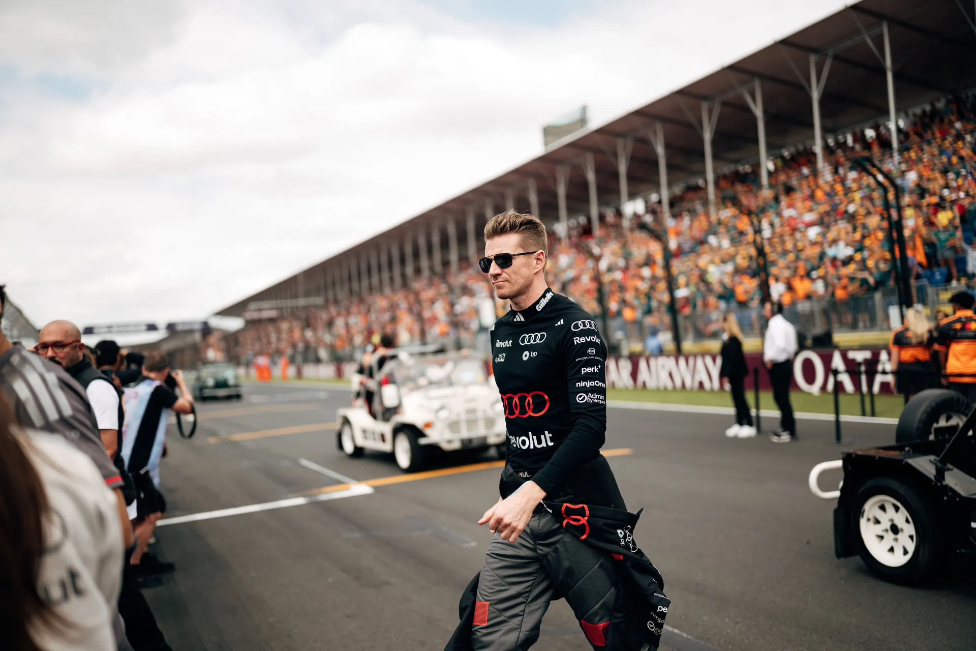 Audi Revolut F1® Team driver Nico Hulkenberg walks through the grid surrounded by marshals, team members, and spectators in Melbourne.