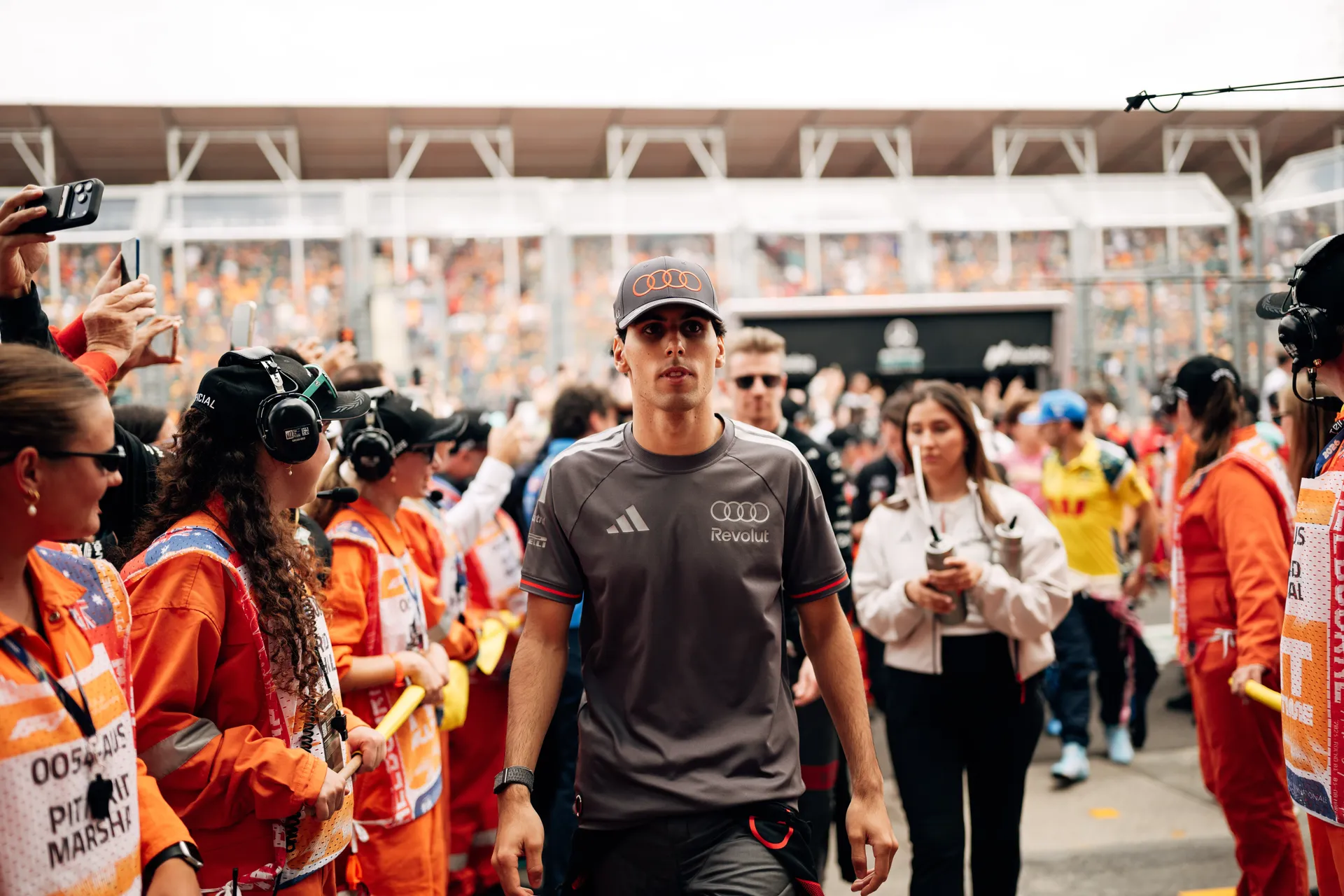 Audi Revolut F1® Team driver Gabriel Bortoleto walks through the grid surrounded by marshals, team members, and spectators in Melbourne.