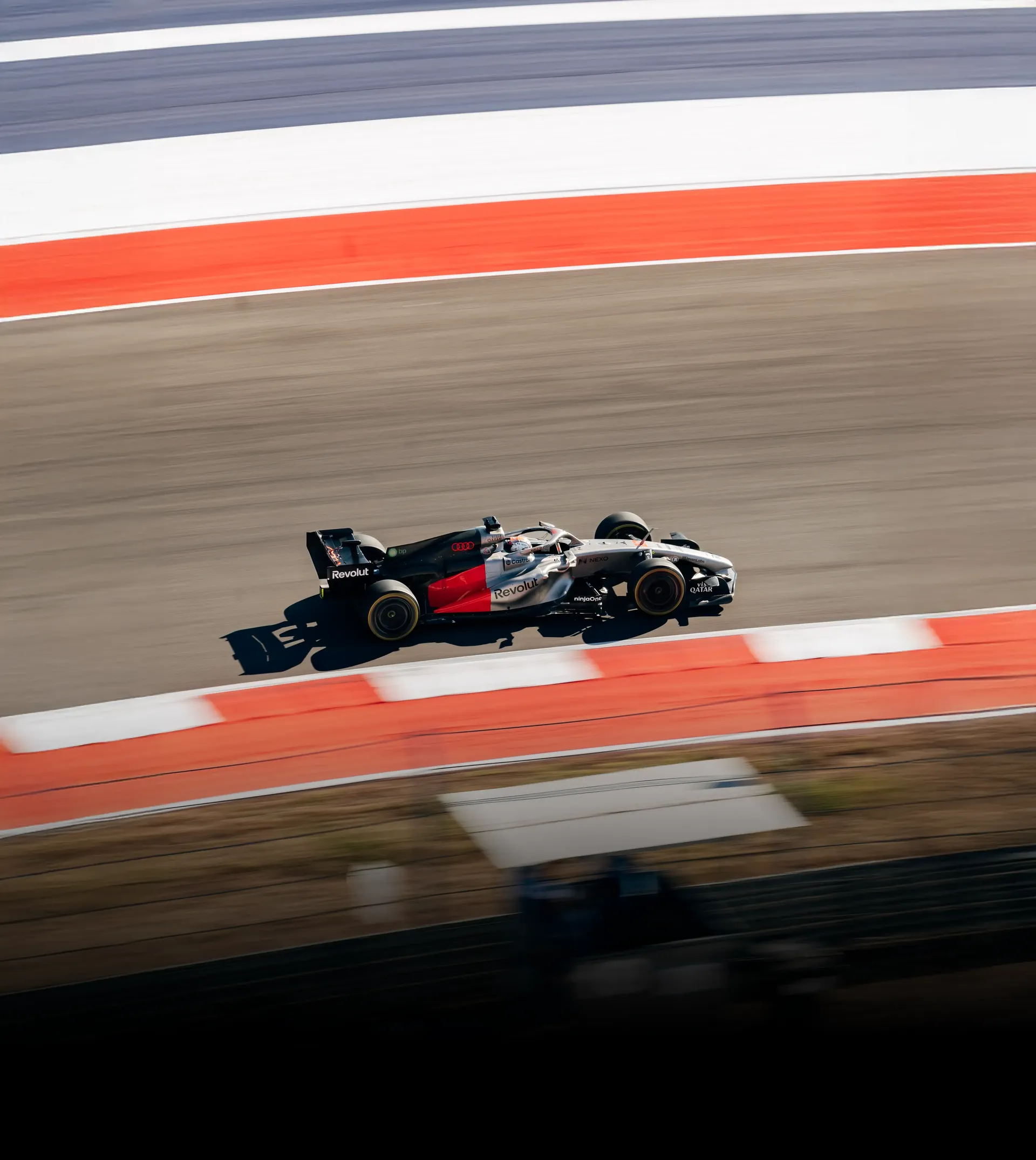 Car of the Audi Revolut F1® Team driving on the track past a red and white kerb, seen from above