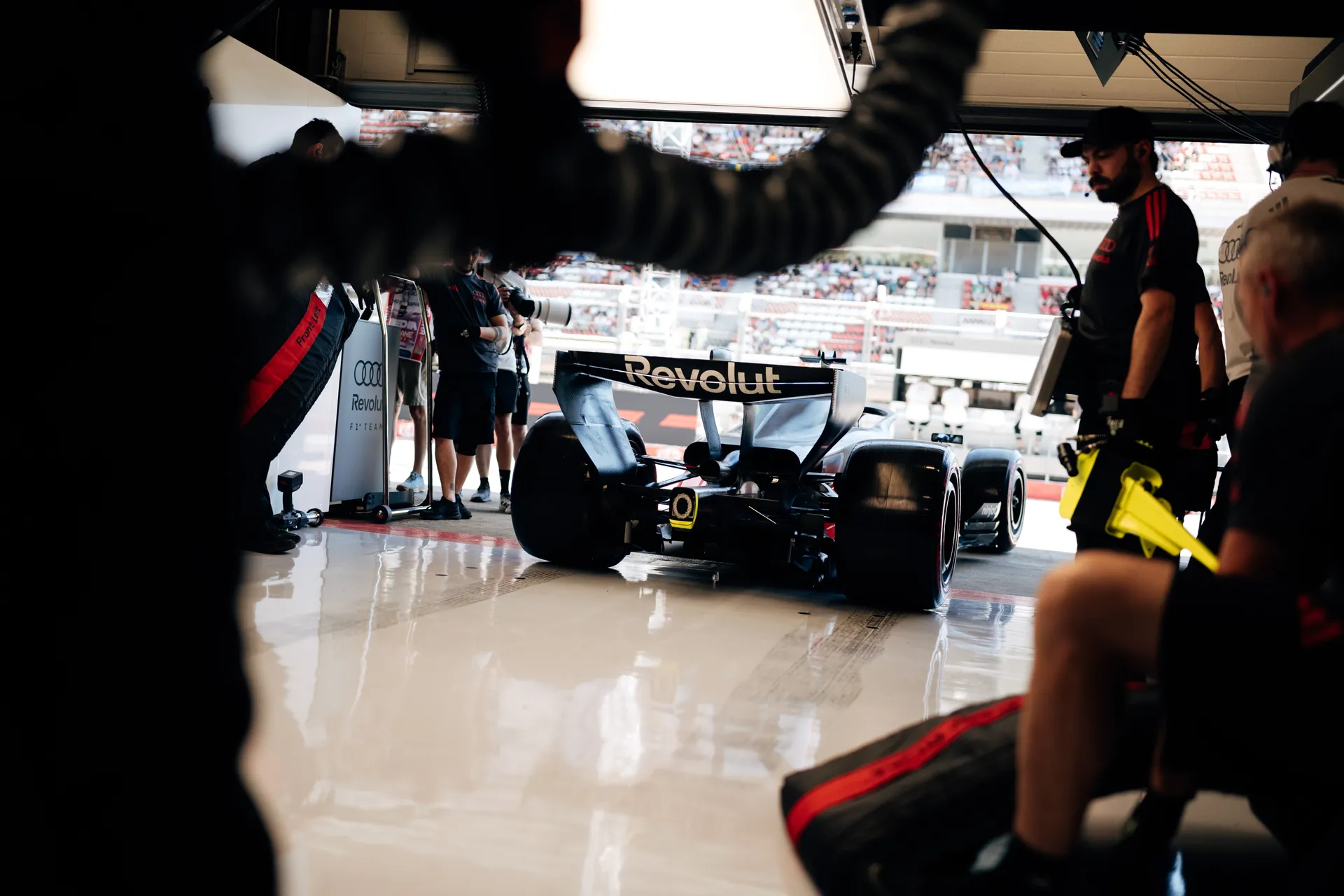Rear view of an Audi Revolut F1® Team car leaving the garage, framed by team members and pit lane activity.