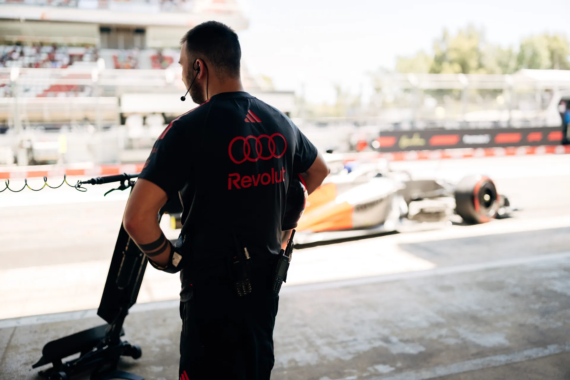 Audi Revolut F1® Team crew member wearing headset monitoring track action as a car passes in the background.