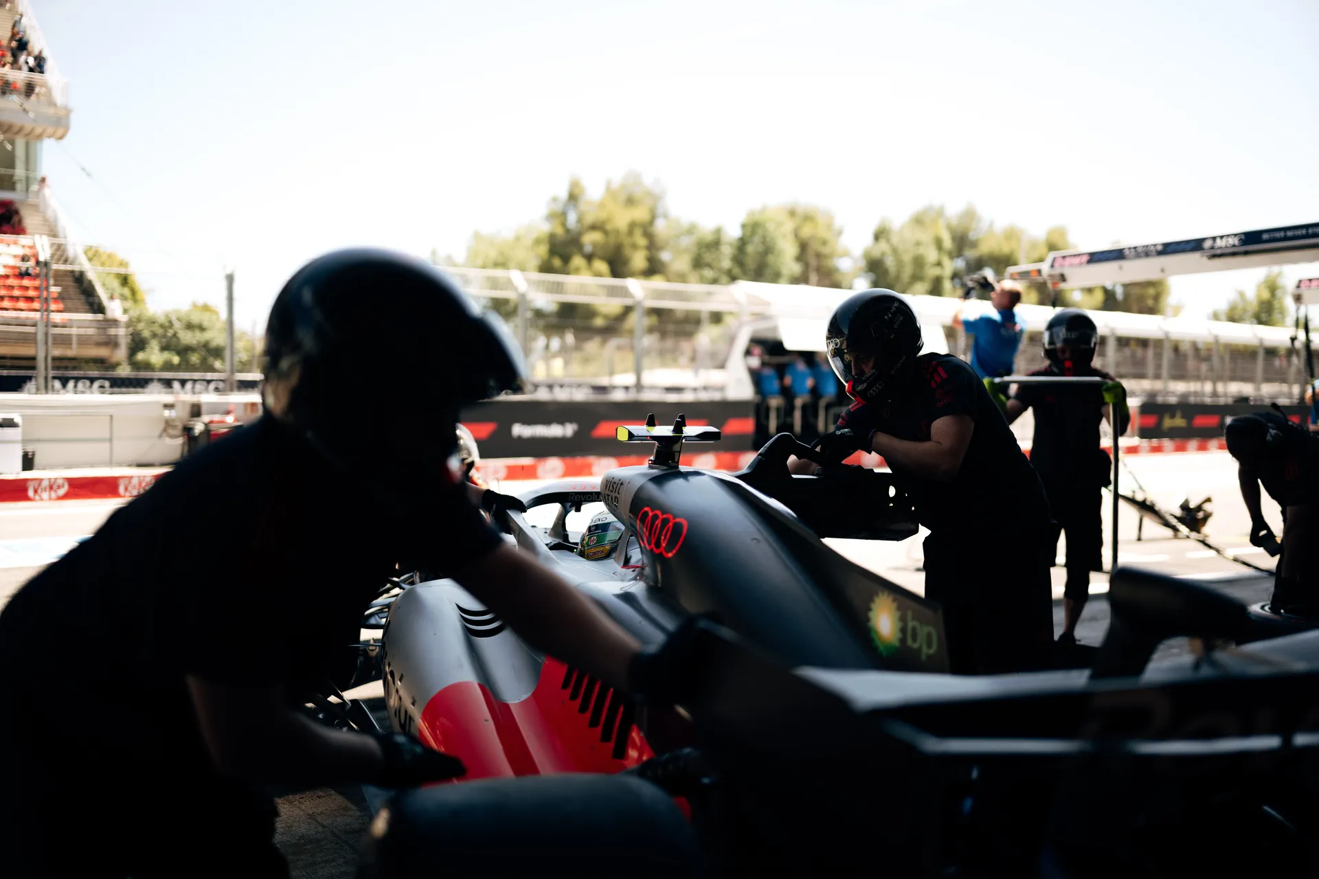 Audi Revolut F1® Team pit crew working on the car during a garage stop, with front wing and nose section in focus.