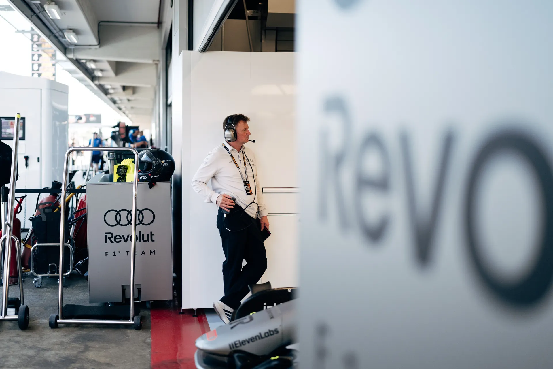 Audi Revolut F1® Team Allan McNish standing beside equipment cabinet with team branding, observing pit lane operations.