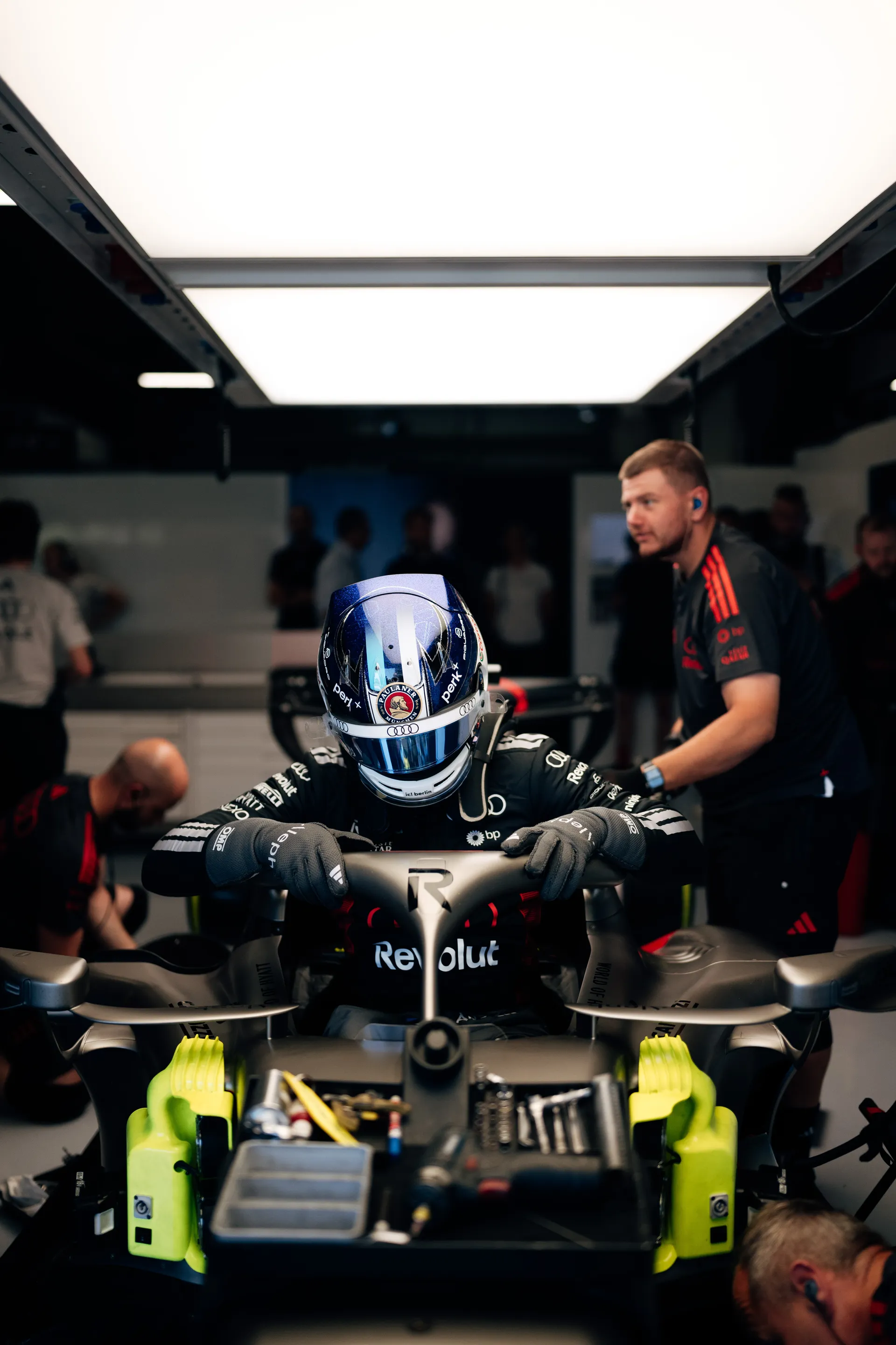 Paul Aron jump out in the Audi Revolut F1® Team cockpit inside the garage, surrounded by mechanics making final adjustments.