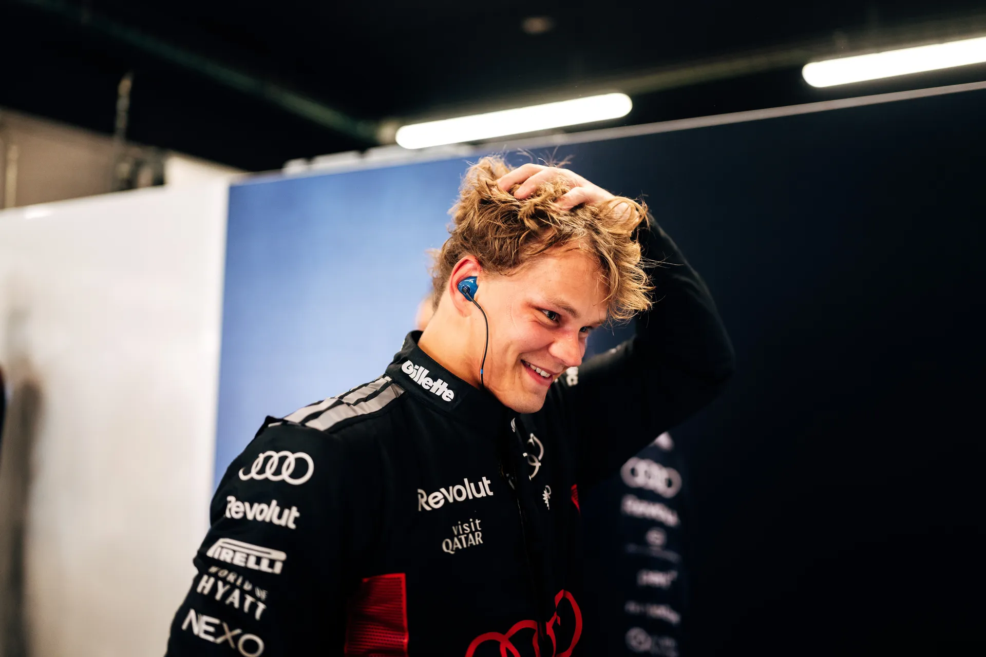 Paul Aron smiling and running his hand through his hair, wearing Audi Revolut F1® Team race overalls.