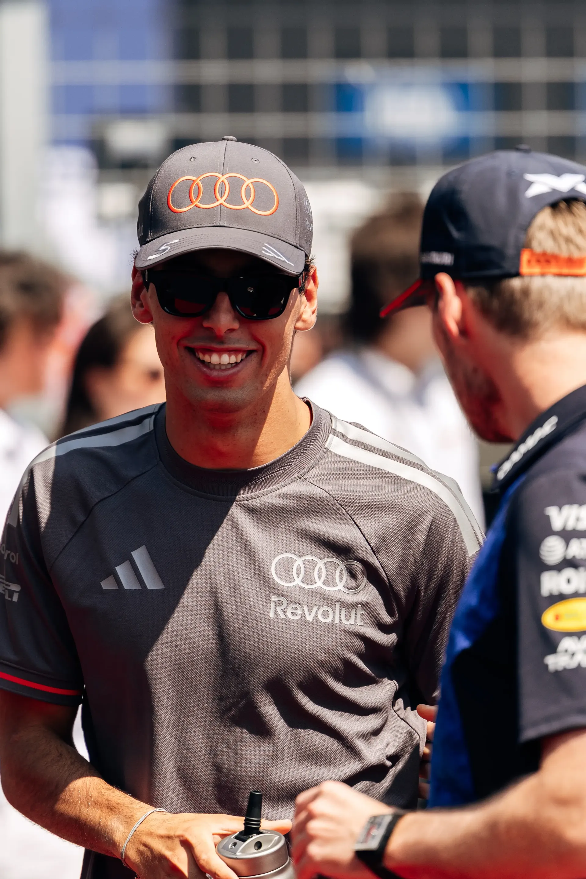 Gabriel Bortoleto smiles while talking with another driver during the drivers' parade at the Hungarian Grand Prix, wearing an Audi Revolut F1® Team cap and team shirt.