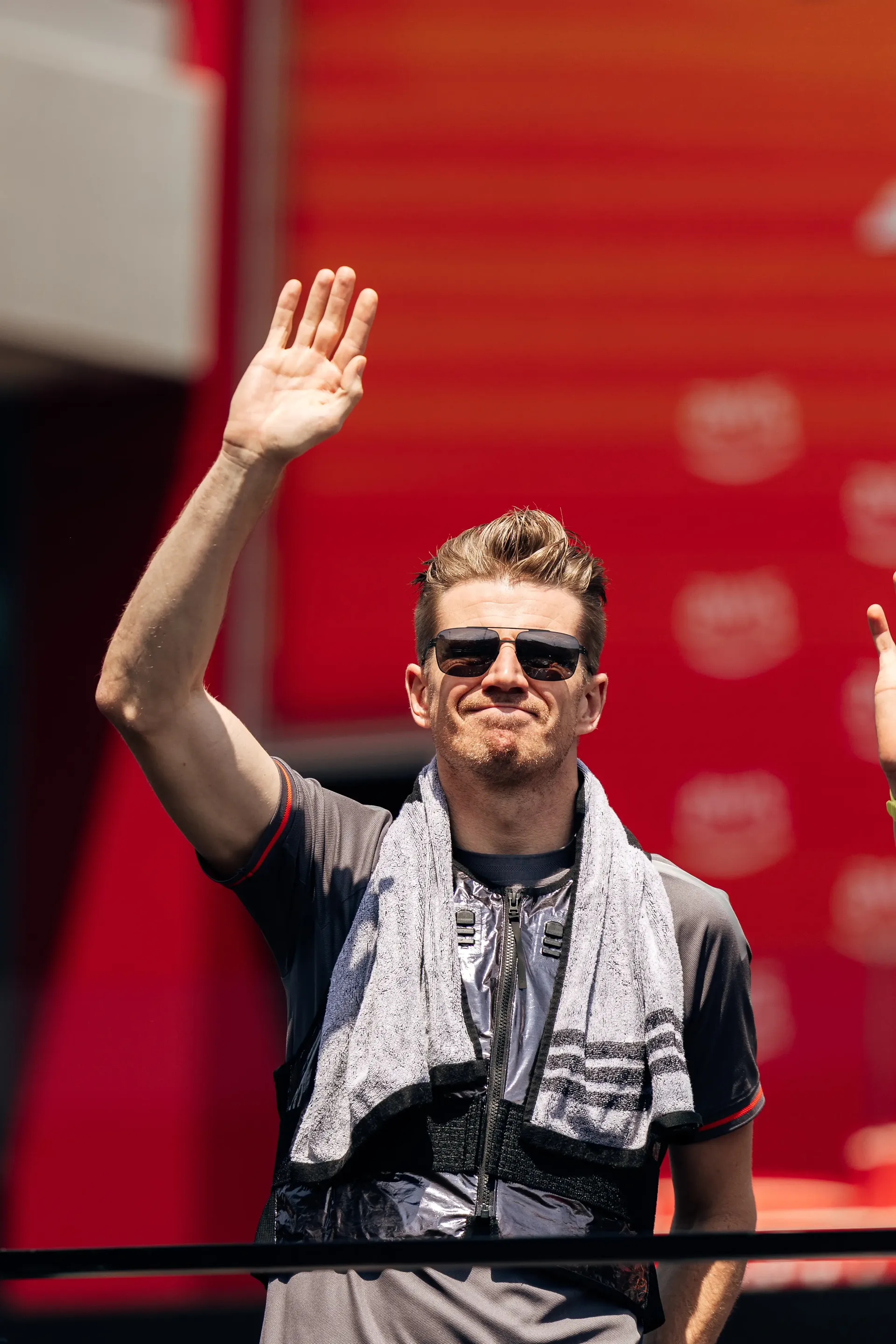 Nico Hulkenberg waves to fans from the drivers' parade vehicle during the Hungarian Grand Prix, wearing an Audi Revolut F1® Team shirt with a towel around his shoulders.