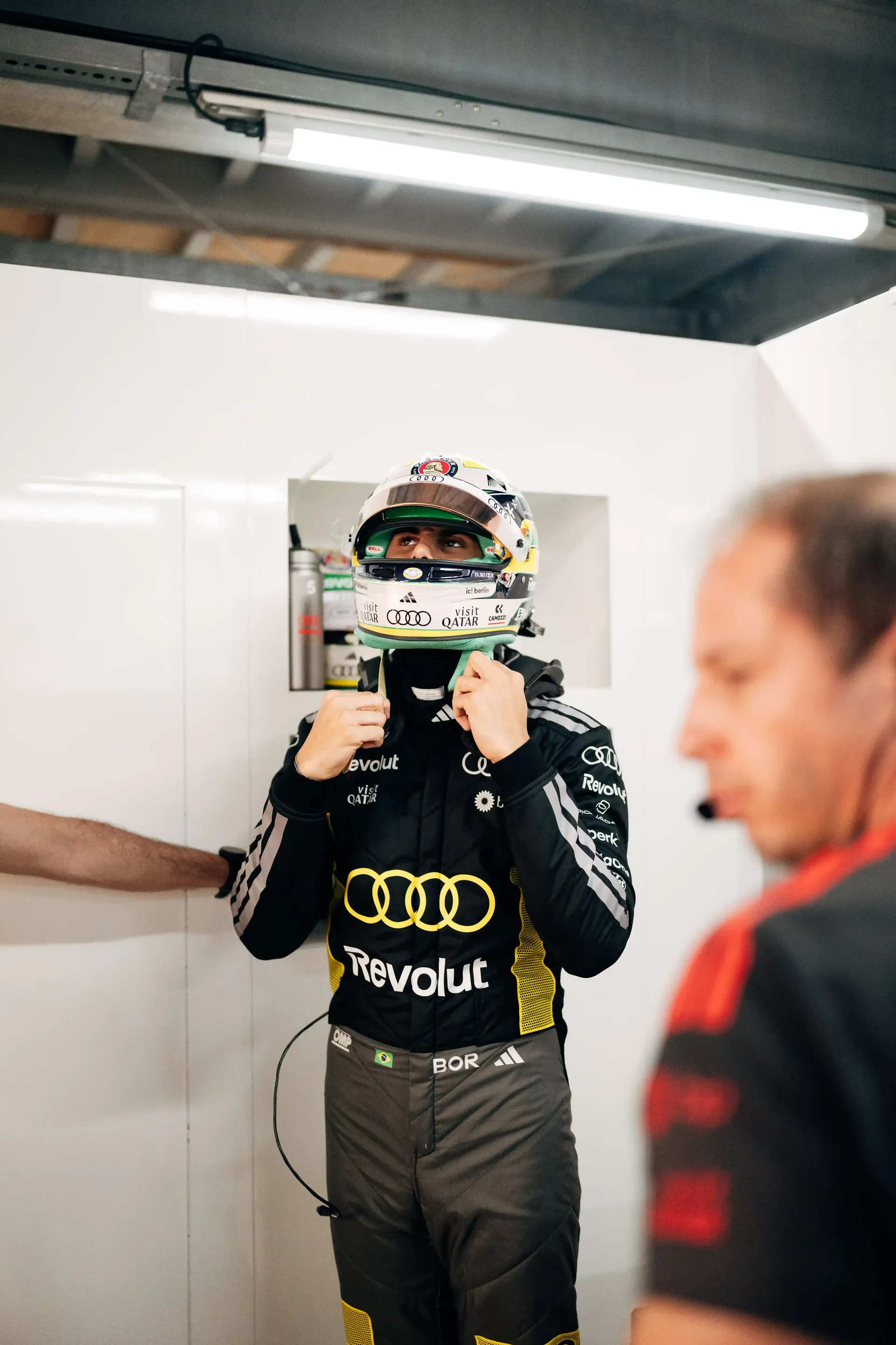 Gabriel Bortoleto driver at Audi Revolut F1® Team in full race suit and helmet stands in the garage during Monaco FP1 preparations.