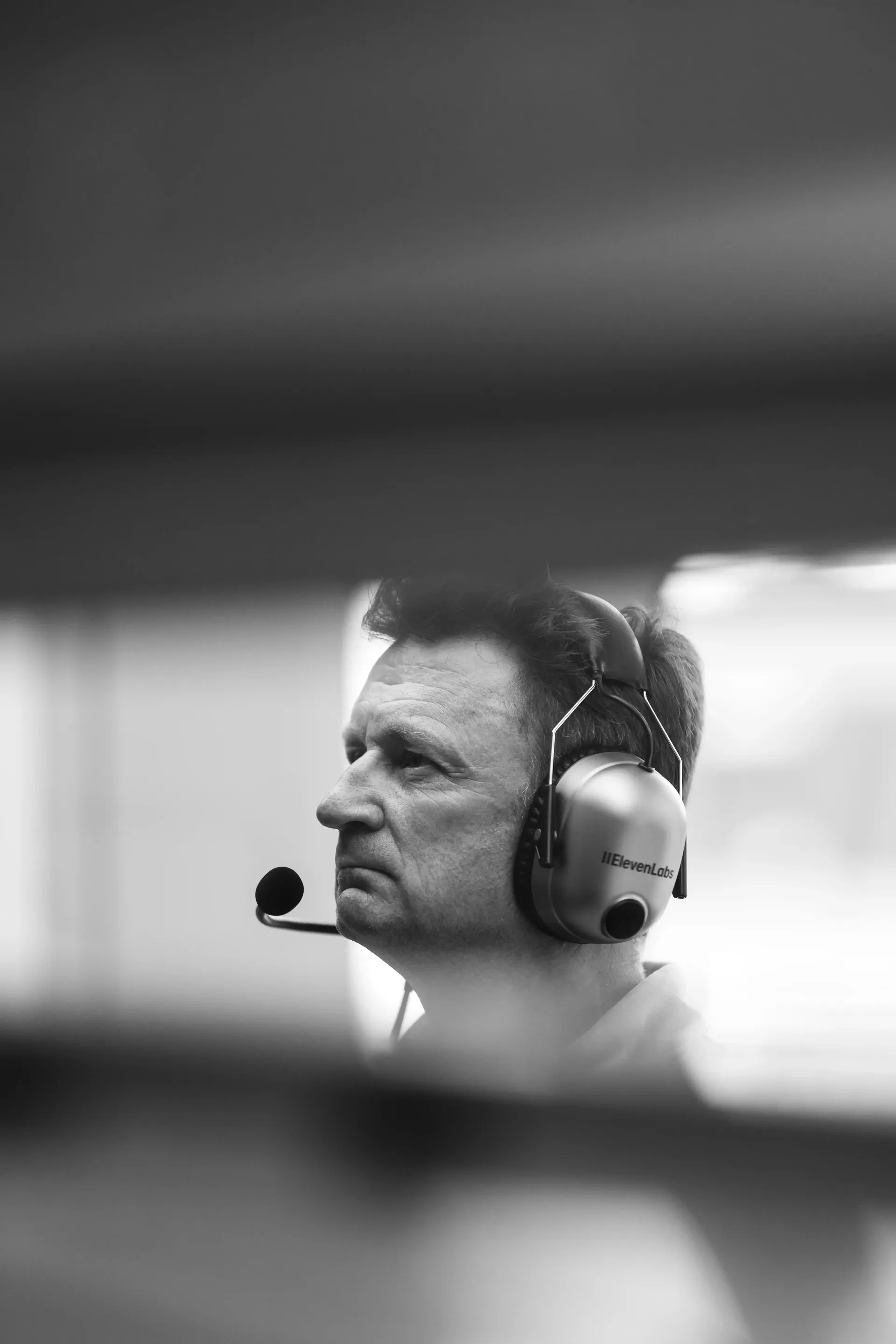 Black-and-white portrait of an Audi Revolut F1® Team racing director Allan McNish wearing a headset and monitoring track activity.