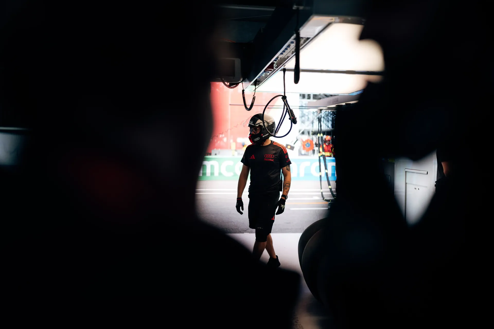 Audi Revolut F1® Team crew member walks through the Monaco garage framed by equipment and shadows.