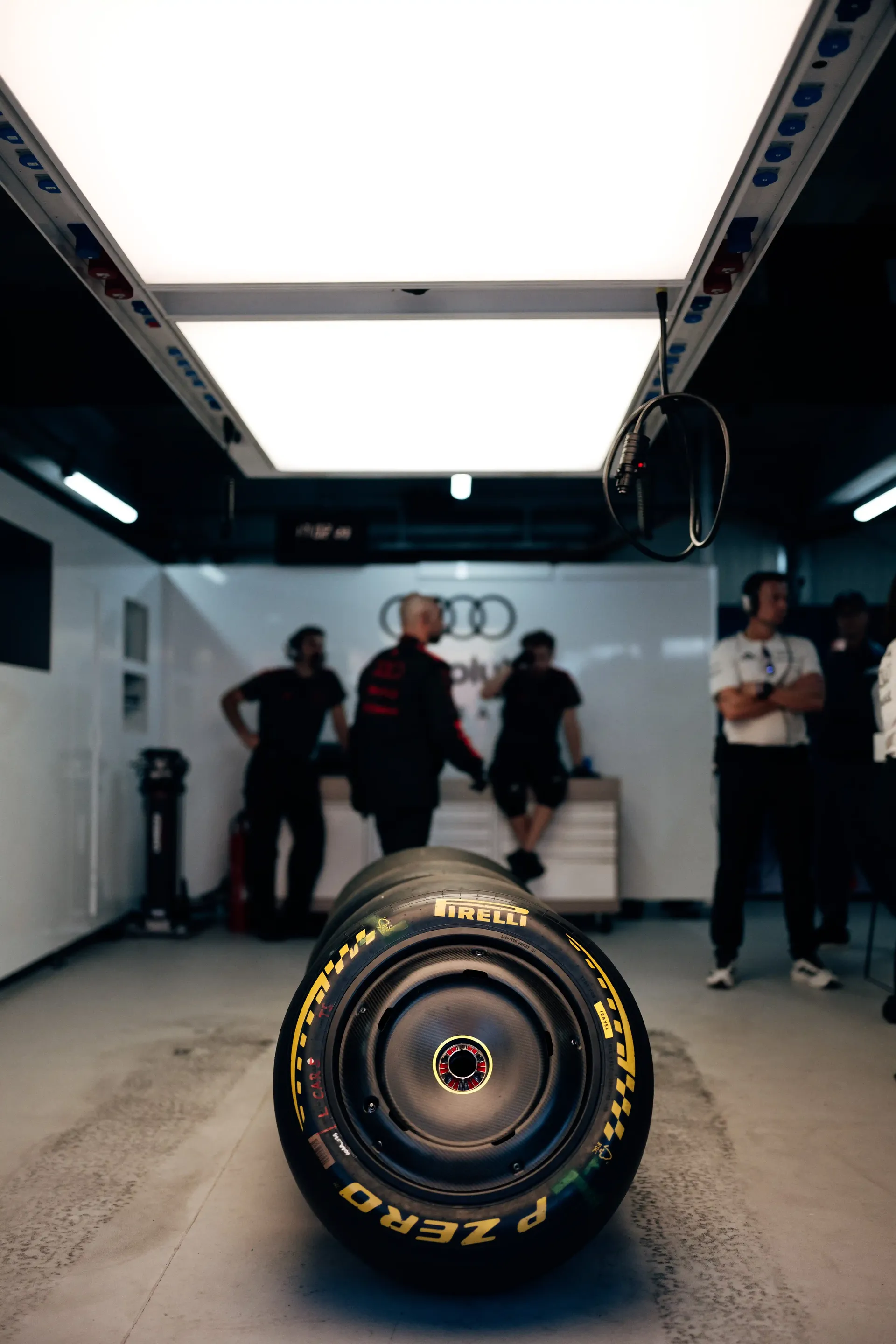 A Pirelli Formula 1 tyre in the foreground of the Audi Revolut F1® Team garage with crew members in the background.