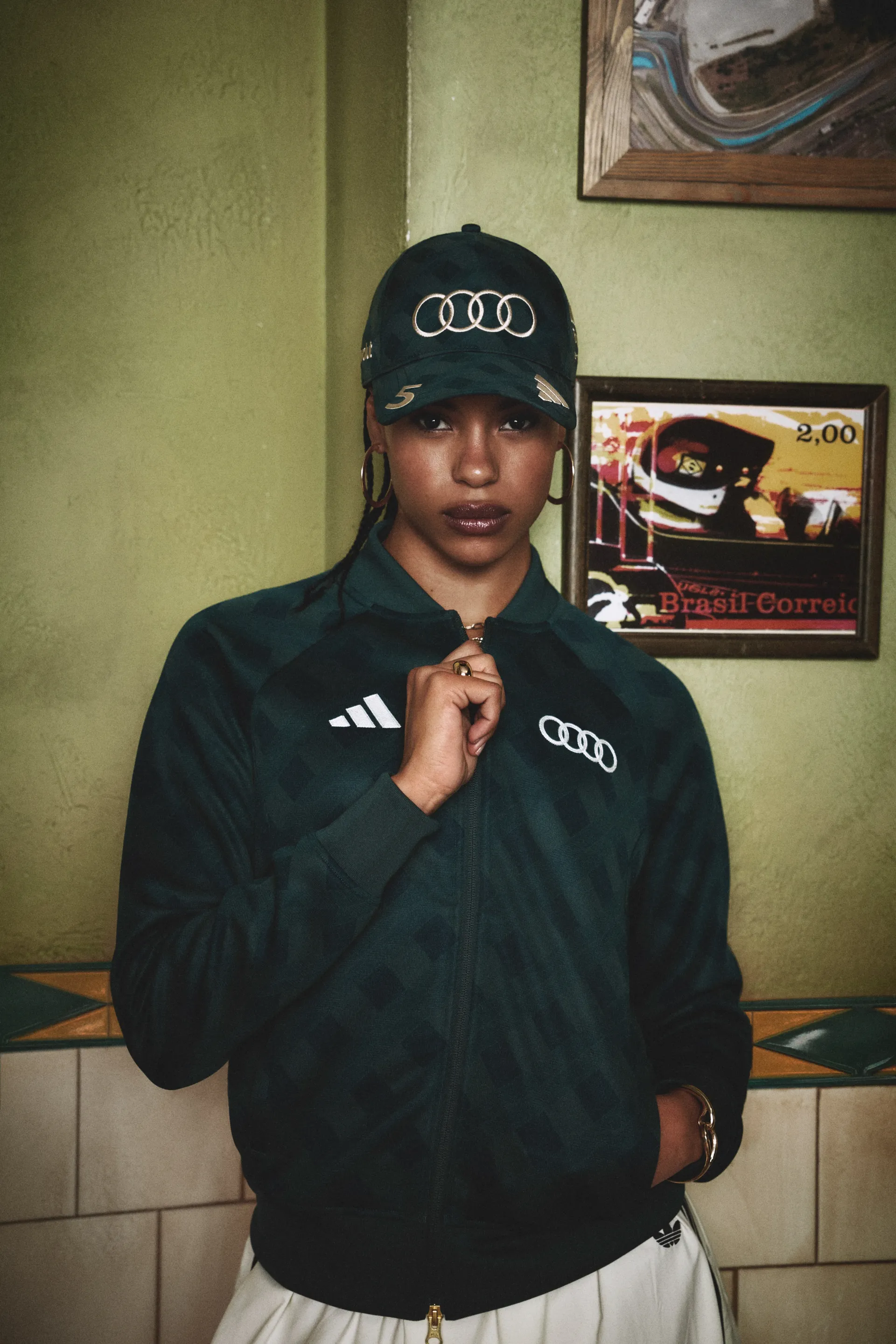 Model in a green Audi cap zipping up a green adidas track jacket, adidas x Audi Revolut F1® Team Sampa Soul collection