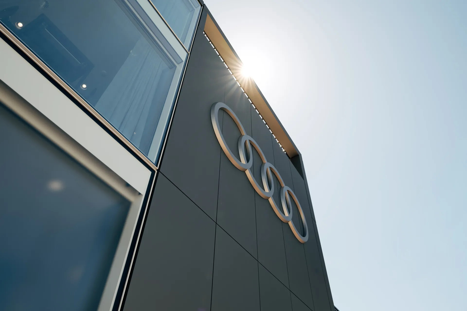 Exterior side-front view of the Audi Revolut F1® Team hospitality hub featuring prominent Audi rings on the façade.