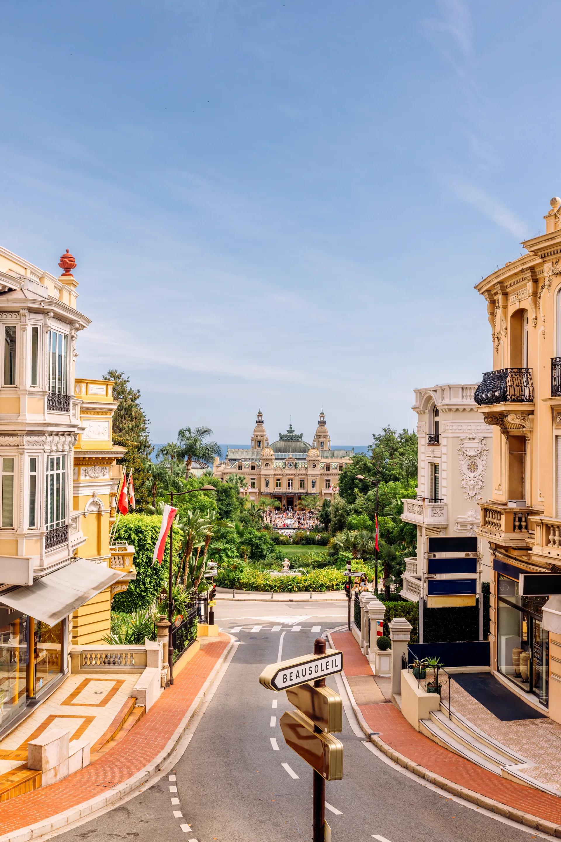 Street in Monaco lined with ornate buildings, leading toward a landmark square under a clear blue sky.