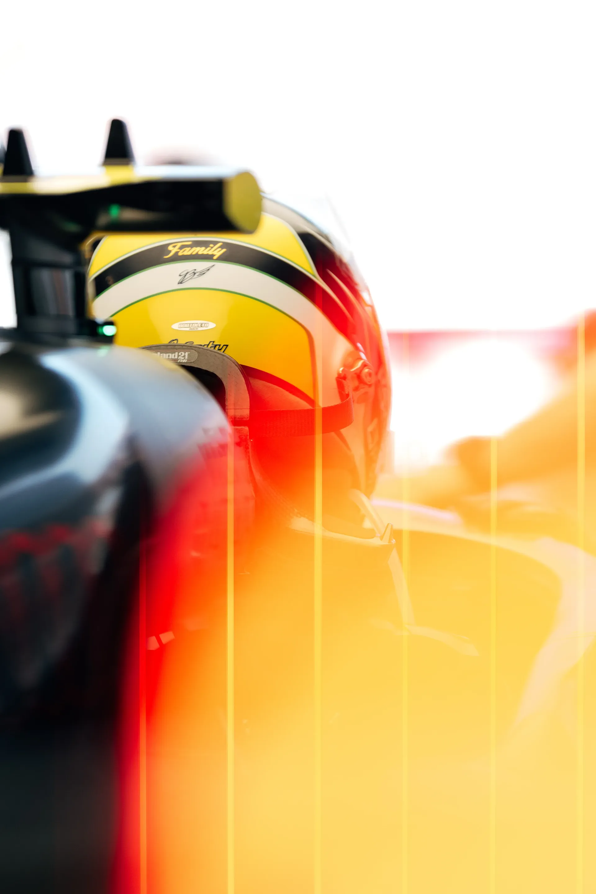 Rear view of an Audi Revolut F1® Team Gabriel Bortoleto driver helmet in the cockpit with warm light flares across the frame.