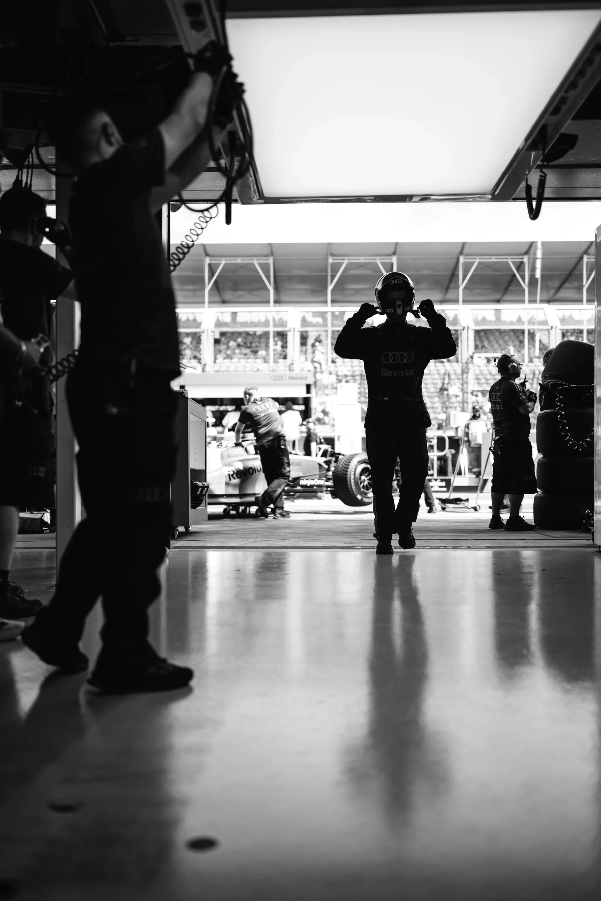 Black and white image of an Audi Revolut F1® Team crew member walking through the garage entrance in full helmet.